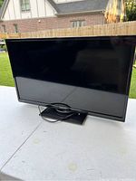 Front view of the Orion SLED2468W 24-inch LED TV showing the screen and base stand on a table outdoors.