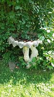 Full view of outdoor bird bath with composite scalloped basin and double seahorse base surrounded by greenery.