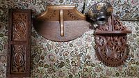 Three wood carved decorative wall shelves and one rectangular carved panel on floral fabric background