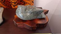 Stone bird carving displayed on an irregular wooden base, showing its smooth rounded body and beak details.