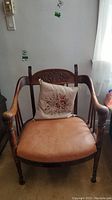 Front view of wood chair with leather seat, carved wooden backrest, and floral cushion.