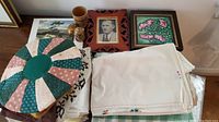 Photo of assorted linens, framed portrait, floral art, round fabric mat, and wooden cups on table