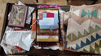 Photo of assorted linens including woven textile, white fabric, quilted pieces, and lace doilies on a wooden table.