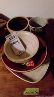 Photo showing six pottery items stacked including bowls, pot, and vase with tag