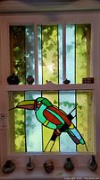 Pottery vases and figurines displayed on a window sill with colorful stained glass background featuring a toucan.