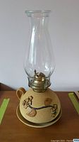 Front view of vintage pottery oil lamp showing glass chimney, pottery base with floral relief, and matching plate