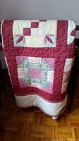 Photo showing folded quilt highlighting patchwork blocks in red, pink, cream, and floral fabrics.