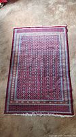 Full view of the small red oriental rug showing overall pattern and condition, placed on carpeted floor.