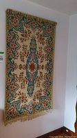 Full view of the vintage tapestry hanging on wall showing overall pattern and condition, some tassels damaged or missing.
