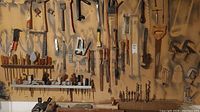 Wide view of many hand tools hung on wall including saws, files, wrenches, hammers, clamps, scrapers, and a wood plane.