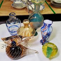 Grouped arrangement of six hand blown glass pieces featuring three vases, one bird figurine, and one apple paperweight with green leaf detail