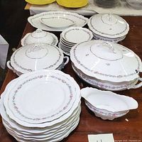 Photograph showing the full assortment of plates, covered serving bowls, tureen, and gravy boat with floral and gold detailed designs.