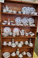 Full shot of wooden shelving unit displaying multiple vintage china tea sets and dishes with floral and gold accents