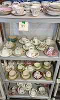 Photo of multiple shelves with various vintage teacups and saucers, floral patterns predominant with gold trim.