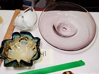 Photo showing three vintage glass centerpiece dishes: a large lavender swirled dish signed underneath, a white dish with a clear handle, and a ruffled-edge blue and amber dish.