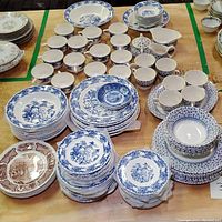 Photo of vintage English ironstone transferware sets with blue and brown transfer designs including plates, cups, and bowls arranged on a table.
