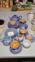 Blue and peach luster Japanese tea service with cups, saucers, plates, teapots, and creamers grouped on table.