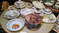 Table with assorted vintage china plates, including Norman Rockwell collector plates, floral patterned plates, and a lusterware teapot