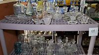 Two shelf levels showing multiple pieces of clear crystal and glass items including candle holders, vases, perfume bottles, and jars