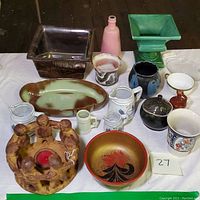 Top-down photo of assorted vintage pottery and porcelain items including bowls, pitchers, vases, and decorative candle holder on white cloth.