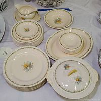 Stack of dinner plates, bowls, small plates, and serving dishes all with yellow rose floral pattern and green-gold trim, arranged neatly on table.
