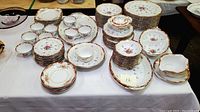 Full view of the large assortment of vintage Sango china including stacked plates, bowls, cups, and saucers arranged on a table with floral patterns and gold trim.
