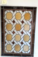 Front view of rectangular stained glass windowpane showing geometric pattern with amber octagonal glass panels and white and clear textured glass sections, surrounded by dark reddish-brown border. One panel is visibly damaged in lower right corner.