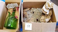 Green glass wine chiller decanter with tassel in a cardboard box alongside another box containing crystal chandelier parts.