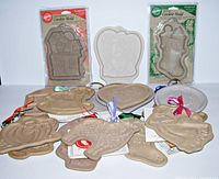 Front view of ten ceramic and stoneware cookie molds, including a haunted house, stocking, heart shapes, and other holiday-themed molds, some in original packaging.