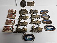 Full lot of 19 vintage metal belt buckles on white background showing all designs grouped by type including trains, ducks, shuttle, and ads.