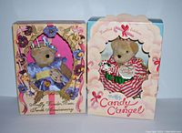 Photo showing two Muffy Vanderbear collectible teddy bears in their original boxes; left bear in blue pansy dress, right bear in candy cane striped angel outfit with wings.