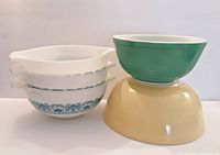 All five vintage Pyrex mixing bowls stacked and shown in profile - green and yellow bowls on the right, white and blue patterned bowls stacked on the left.
