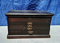 Front view of the antique wooden tool chest showing four drawers with metal handles and a hinged top lid