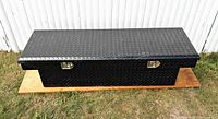 Full view of black truck storage box closed, showing diamond plate pattern and two locks on front