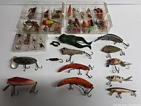 Photo showing full lot of vintage fishing lures and flies in clear plastic compartment trays plus loose lures including frog-shaped and crankbaits.