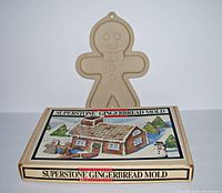 Gingerbread man cookie mold standing upright in front of gingerbread house mold box with colorful illustration