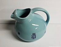Front view of the vintage light blue ceramic pitcher showing rounded body, curved handle and blue tulip decoration