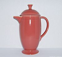 Front view of the rose colored ceramic coffee pot with lid, showing the spout and handle.