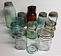 Overview of all 10 vintage glass Mason jars showing variety in size, shape, lid type, and glass color. Several have wire bail lids, some with metal screw lids, and some without lids.