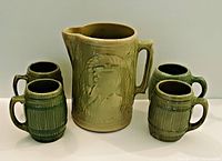 Front view of pitcher and all four mugs showing sea captain and barrel-shaped mugs