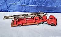 Side view of the red vintage metal toy fire ladder truck with cab and folded extendable ladder, showing length and detailing including S.F.D. marking.