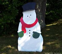 Assembled snowman metal yard decoration displayed outdoors, showing white body, black hat, red scarf, and green mittens on arms.