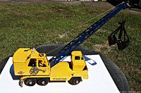 Side view of yellow and black Ny-Lynt Michigan Crane toy truck with blue boom and clamshell scoop bucket attached by string.