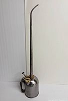 Side view of vintage metal oil can with long narrow spout and pump handle, showing overall shape and length.