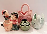 Five vintage pottery pieces including a boy and girl planter pair, green flower frog vase, pink basket planter, and swan planter.