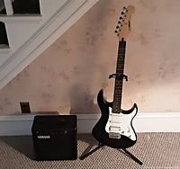 Photo of Yamaha black electric guitar standing on a black guitar stand beside a Yamaha amplifier