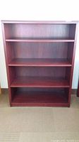 Front view of the faux wood bookcase showing four shelves and reddish-brown color.
