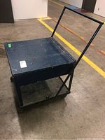 Front angled view of black industrial metal cart showing its top shelf, handle, and wheels.