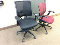 Two office chairs, one black and one red, viewed from the side showing mesh backs and cushioned seats.