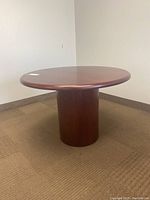 View of the circular wood veneer table showing the full tabletop and cylindrical base.